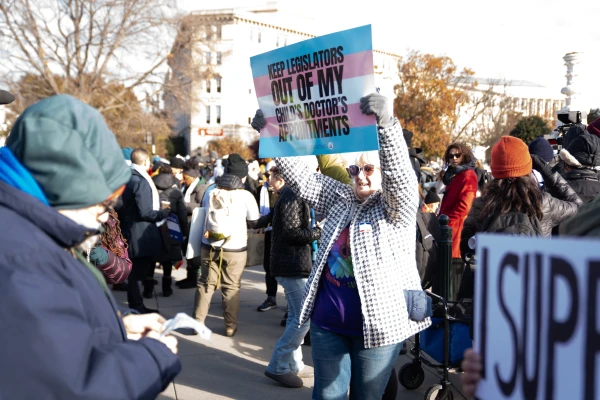 A trans-rights activist holds a sign in support of gender transition for minors at a rally that shared the space outside the nation’s highest court with opponents of “gender-affirming care” for children on Dec. 4, 2024. Credit: Migi Fabara/CNA