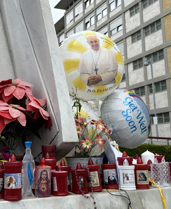 Candles, flowers, and handwritten notes wishing Pope Francis a swift recovery stand underneath a towering statue of St. John Paul II on Feb. 25, 2025, outside Gemelli Hospital in Rome.&nbsp;. Credit: Courtney Mares/CNA