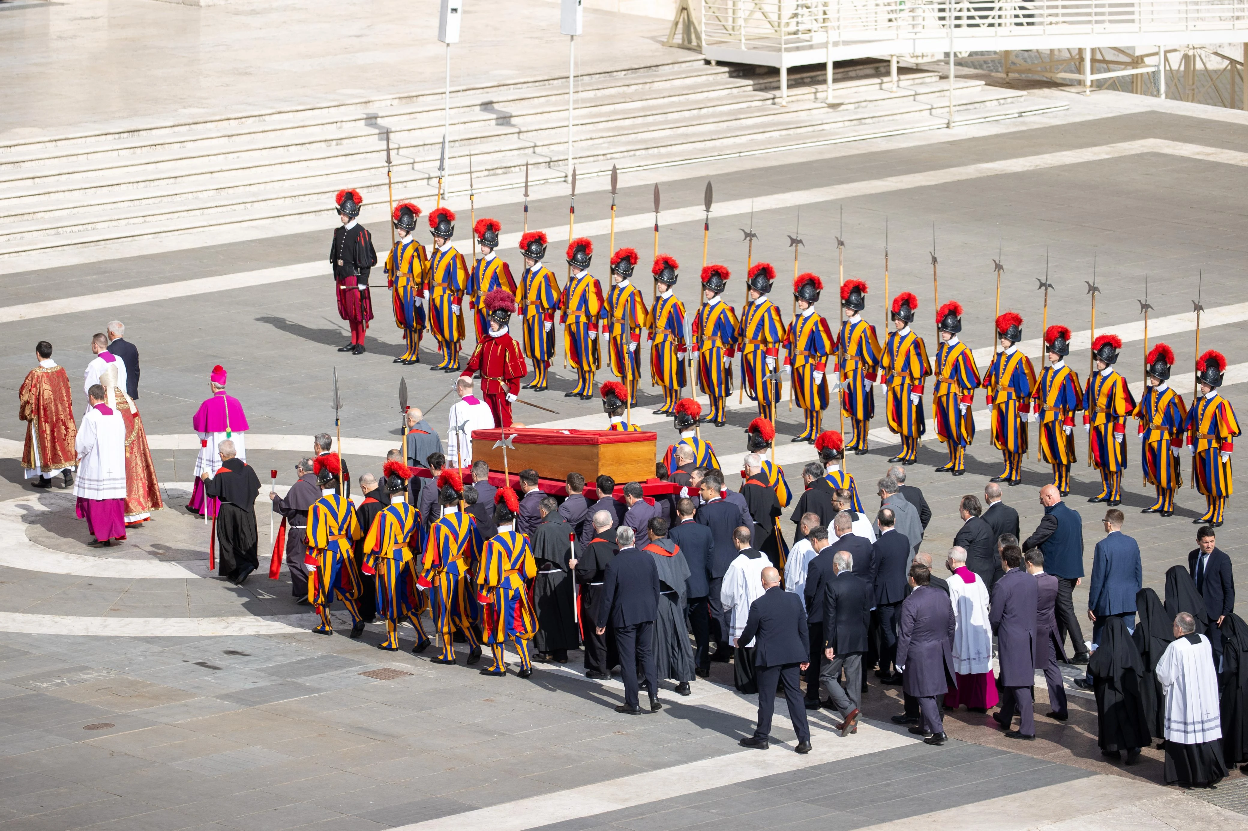 Cardinals, bishops, and Vatican officials walk alongside Pope Francis’ coffin in St. Peter’s Square on April 23, 2025, during the solemn transfer as Swiss Guards stand in formal formation. Credit: Daniel Ibáñez/CNA