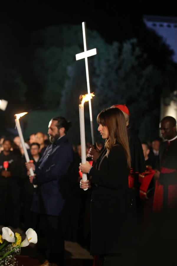 A young woman carries the cross during Rome's Way of the Cross ceremony at the Colosseum while clergy members and faithful follow with candles on Good Friday, April 18, 2025. Credit: Zofia Czubak / EWTN News