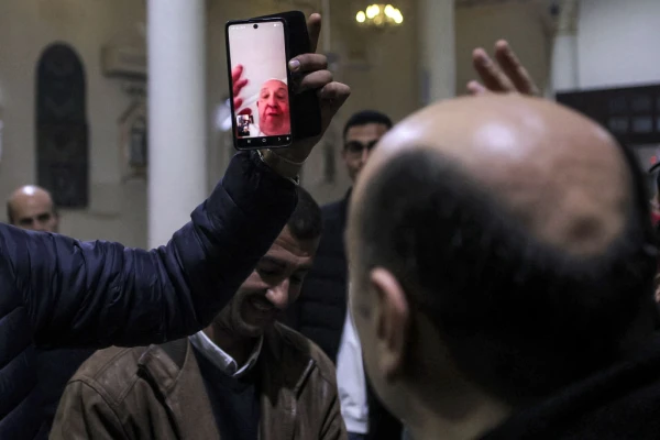 A man holds up a phone for Father Gabriel Romanelli, parish priest of the Roman Catholic Church of the Holy Family in Gaza, to have a video conference call with Pope Francis as the latter blesses the congregation during Christmas Eve Mass at the church in the Zaytoun neighbourhood of Gaza City on Dec. 24, 2024, amid the ongoing war in the besieged Palestinian territory between Israel and Hamas. Credit: OMAR AL-QATTAA/AFP via Getty Images