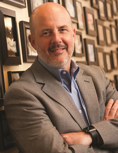 Dr. Christopher Stroud in front of a wall of photos of babies that would not exist without his clinic. Credit: Photo courtesy of Dr. Christopher Stroud