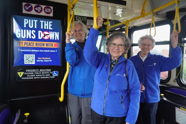 (Left to right) Sister Patricia “Pat” Dowling, Sister Elaine Davia, and Sister Nancy Glynn stand inside a Baltimore city bus where the “Put the Guns Down” ads will also appear. Credit: Liz O’Neill