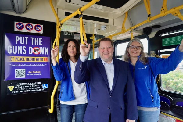 (Left to right) Rhonda Hooker, Nicholas Stein, and Simone Blanchard — members of the Sisters of Bon Secours Justice, Peace, and Integrity of Creation team — stand on a Baltimore bus with the “Put the Guns Down” campaign ads. Credit: Liz O’Neill