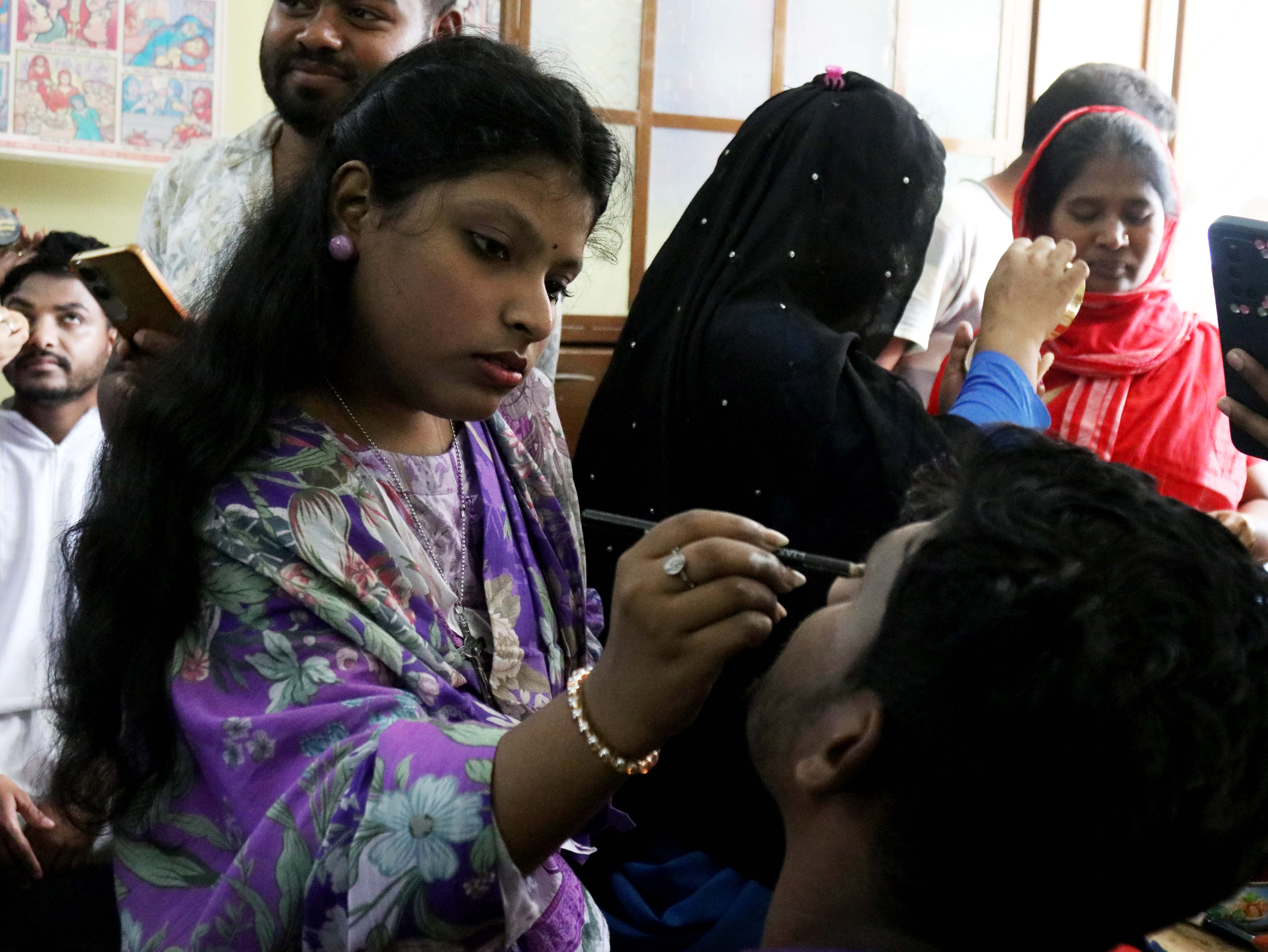 A parishioner applies makeup to a participant ahead of a living Way of the Cross at the Jesus Worker Center in Gazipur, Bangladesh, Friday, April 3, 2026. | Credit: Stephan Uttom Rozario