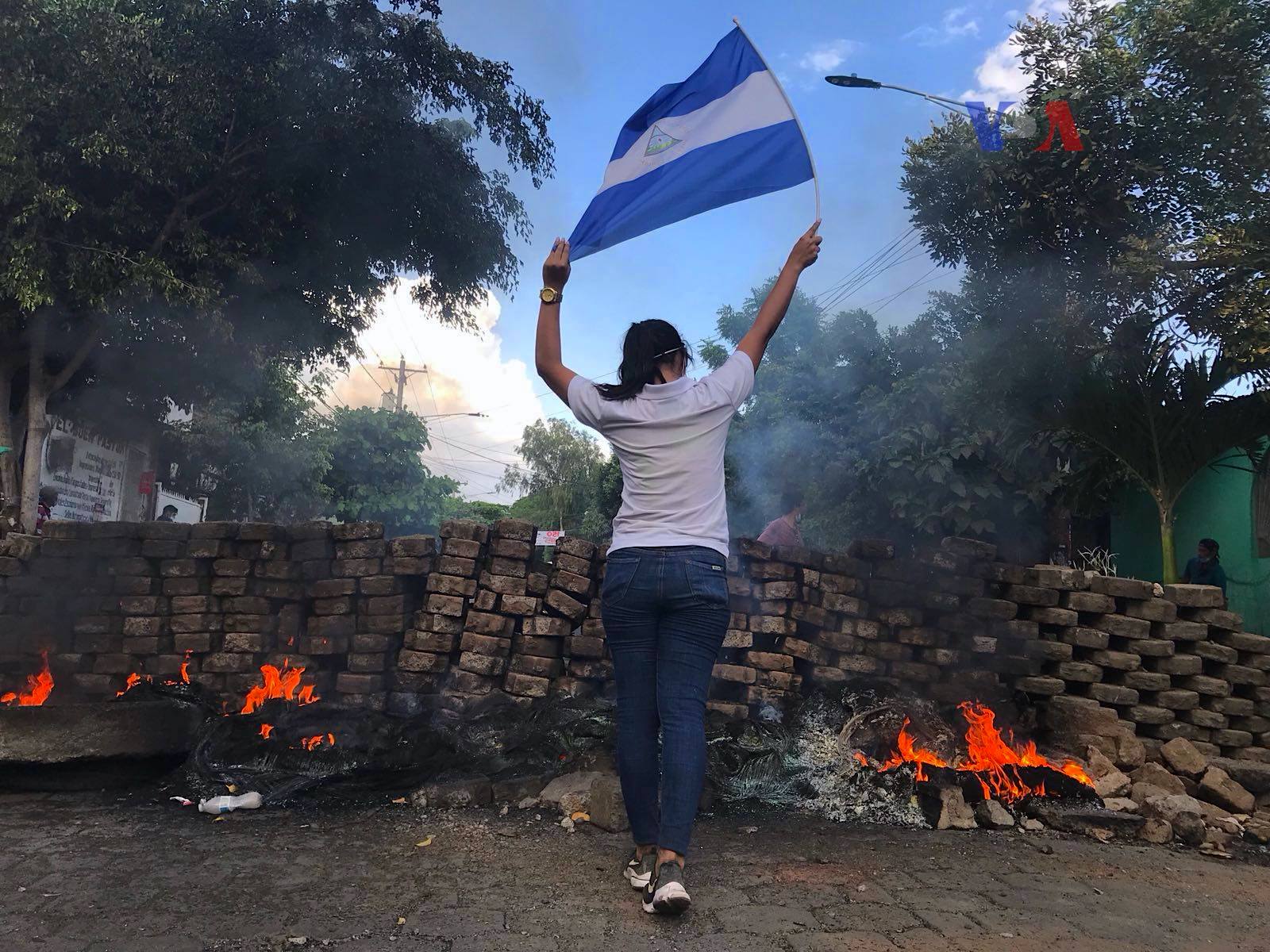 A young woman holds aloft a Nicaraguan flag near a barricade against police during the protests of April 20, 2018, in Nicaragua. | Credit: Voice of America/Public domain