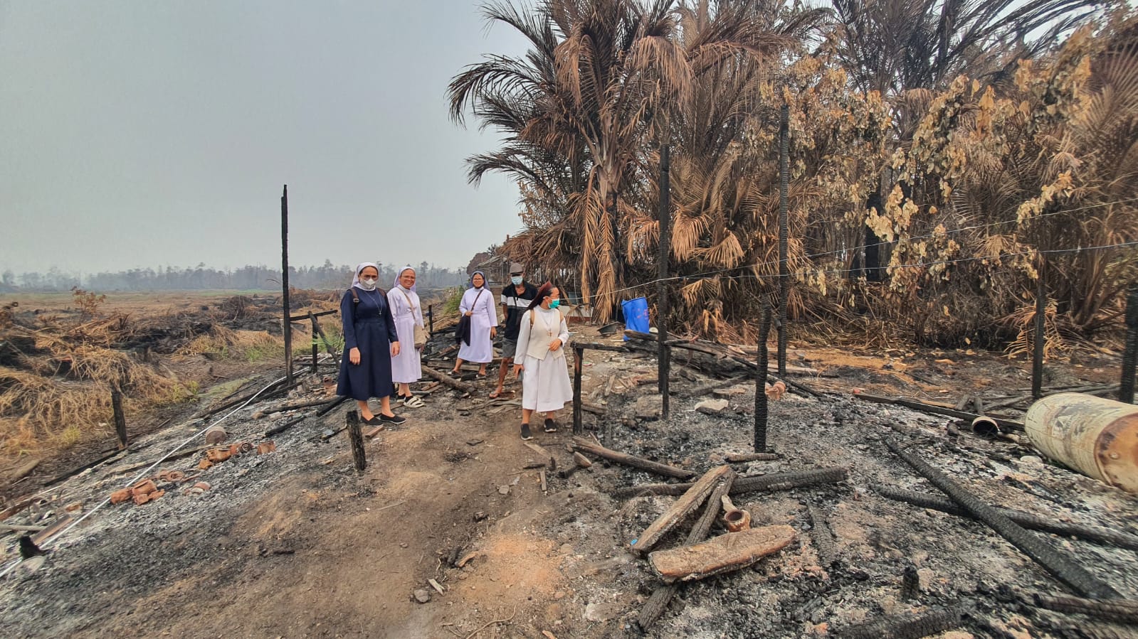 Catholic sisters and volunteers stand at the site of a house destroyed by forest and land fires in Kalimantan, 2026. | Credit: Photo courtesy of Friar Taucen Girsang, OFM
